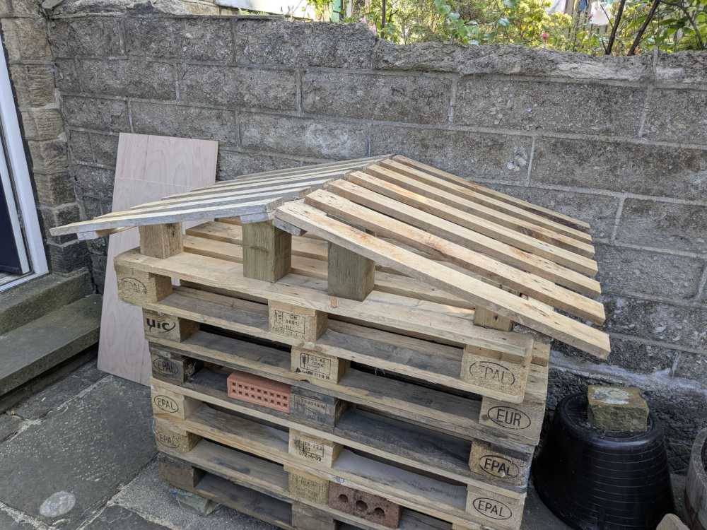 A stack of pallets with a wooden frame on top for a pitched roof